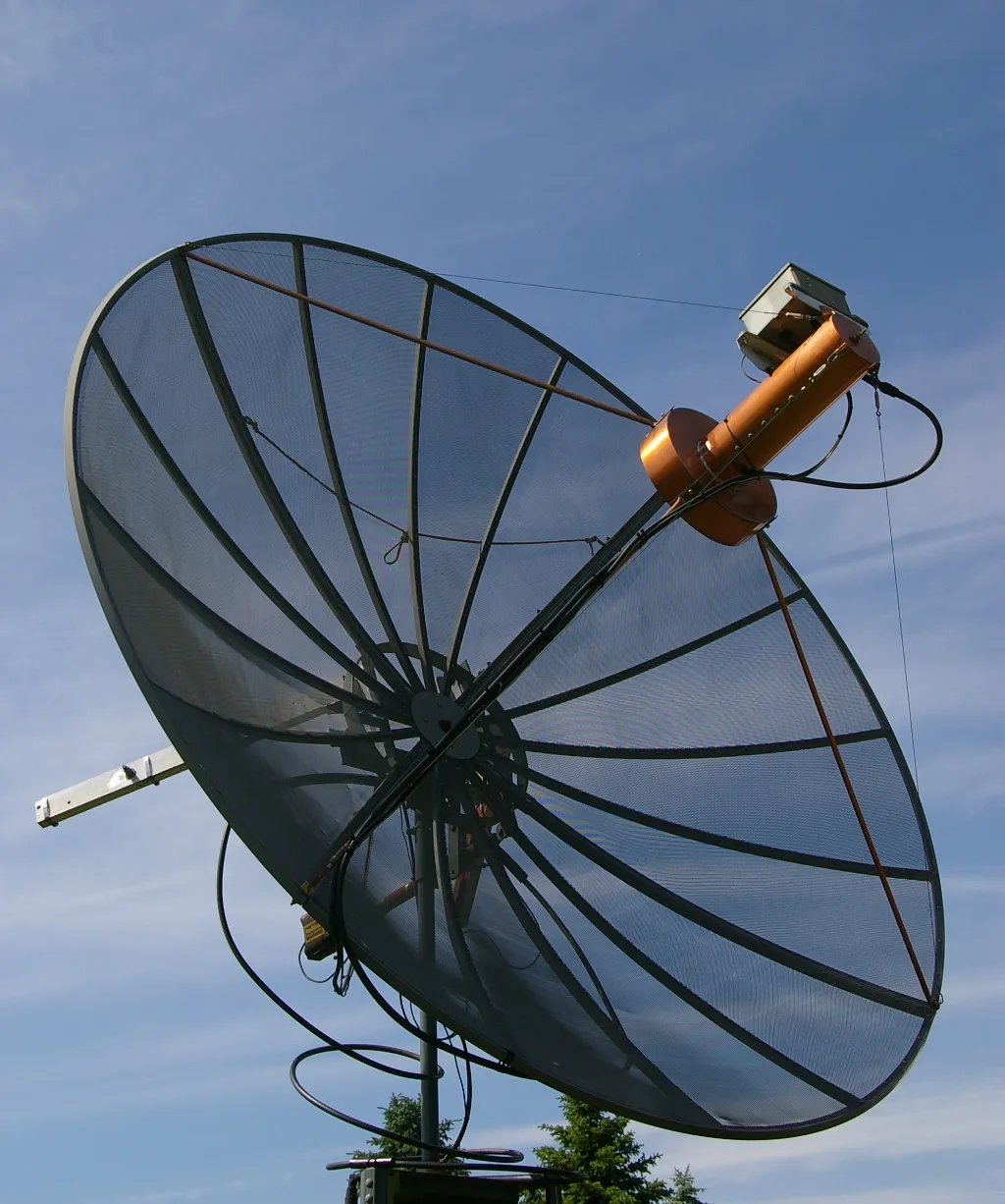 A large mesh dish antenna at the VA7MM moonbounce station points skyward against a blue sky, ready for Earth-Moon-Earth contacts.